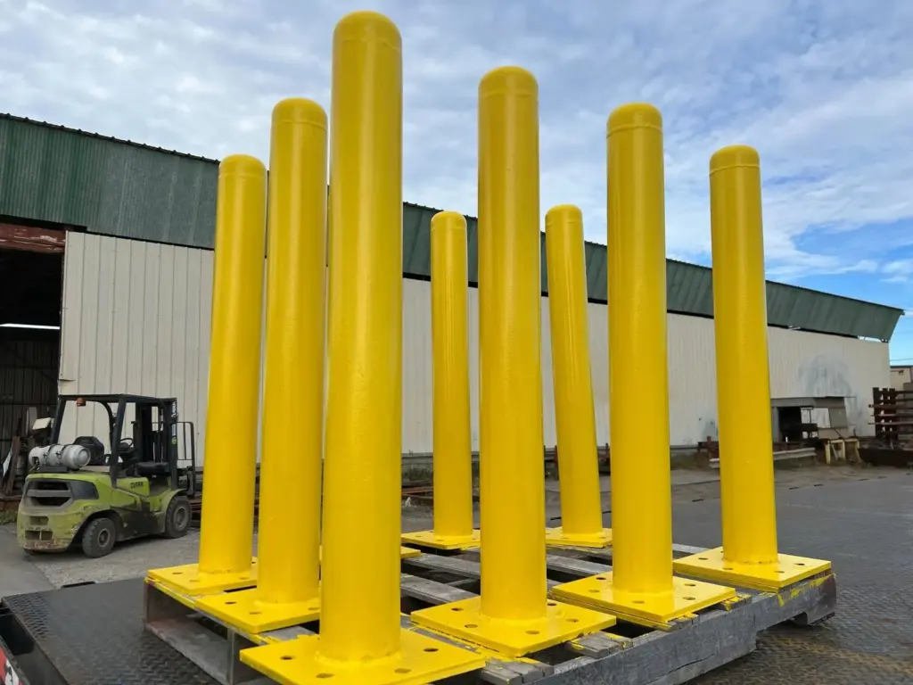 Yellow steel pipe bollards with welded base plates palletized in the Surplus Steel yard